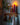 This image shows a shelf with hooks upon which sits a Greentree Petite Pillar candle in Red, lit. It sits amongst other wintery items.