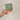 Hand holding a plantable seed paper envelope with floral design on a beige background
