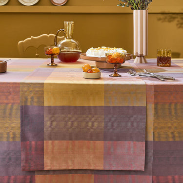 Table setting with a plaid tablecloth, fruit, and glasses against a yellow wall.