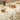 Dining table set with floral tablecloth, plates, and candles in a cozy indoor setting.