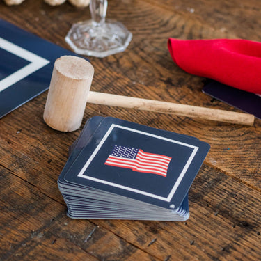 Stack of cards with American flag design on a wooden table with a mallet and other items.