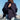 Woman wearing a dark blue poncho by a waterfront with boats in the background