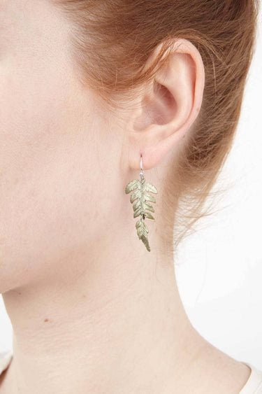 Close-up of a person wearing a leaf-shaped earring on a white background