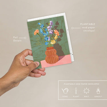 Hand holding a plantable seed paper envelope with floral design on a beige background