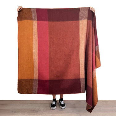 Person holding a large plaid blanket with red and brown colors on a white background