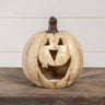 Decorative pumpkin with a carved face on a wooden surface against a white wall.
