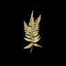 A single metallic gold fern leaf pendant or brooch centered on a solid black background.