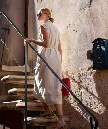 Woman in a white dress standing on stone steps with a textured wall background