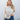 Woman wearing a beige knitted sweater and blue jeans against a white wall.