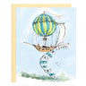 Airship dirigible features a brightly colored yellow and blue striped balloon carrying the ship aloft. Bunting hanging off the ship reads “Happy Birthday”