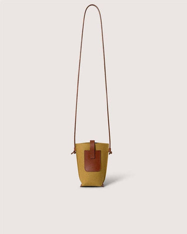 A mustard yellow canvas bucket bag with brown leather trim and a long brown shoulder strap, shown against a solid light beige background.