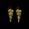 A pair of gold-toned dangle earrings shaped like fern fronds, shown against a solid black background.